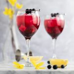 A couple glasses of blueberry gin cocktails, next to lemon slices and blueberries.