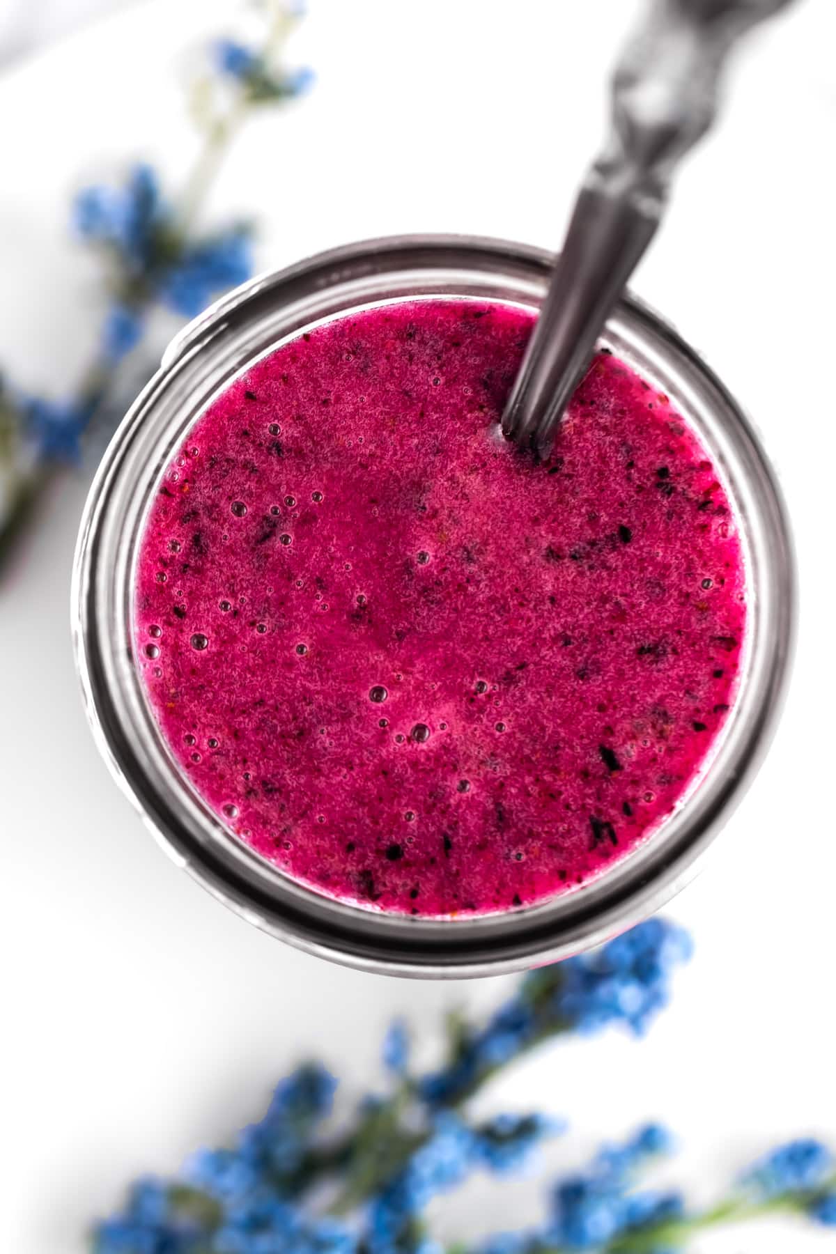 Overhead view of a mason jar of pinkish-purple blueberry glaze on a white table.