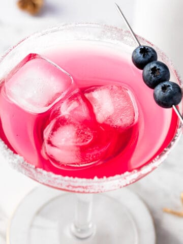 A blueberry lemonade margarita garnished with blueberries on a white background.