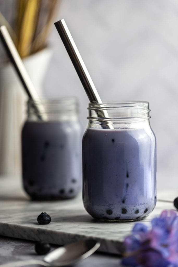 Two jars of blueberry milk tea with boba and metal straws on a grey marble board.