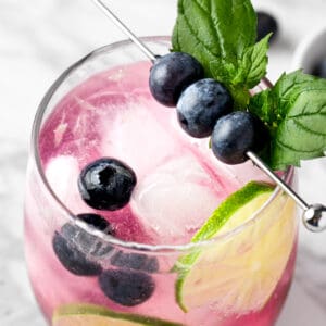 A blueberry mojito mocktail garnished with fresh blueberries and lime wheels.