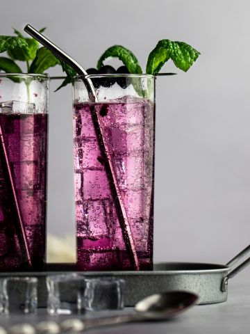A couple of blueberry mojitos with mint and blueberry garnish, lined up on a metal serving tray.