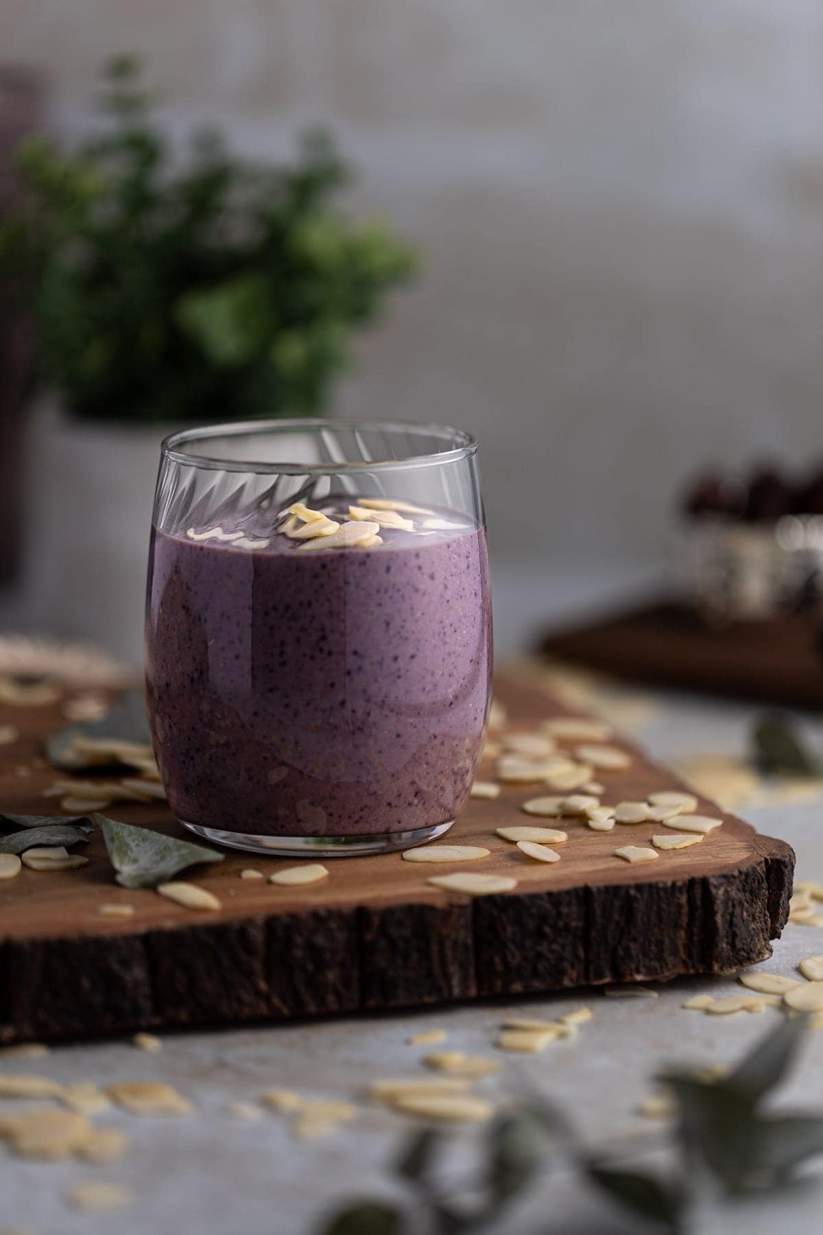 Up close view of a vegan blueberry tahini smoothie on a wooden board, with sliced almonds scattered on the table.