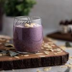 Up close view of a vegan blueberry tahini smoothie on a wooden board, with sliced almonds scattered on the table.