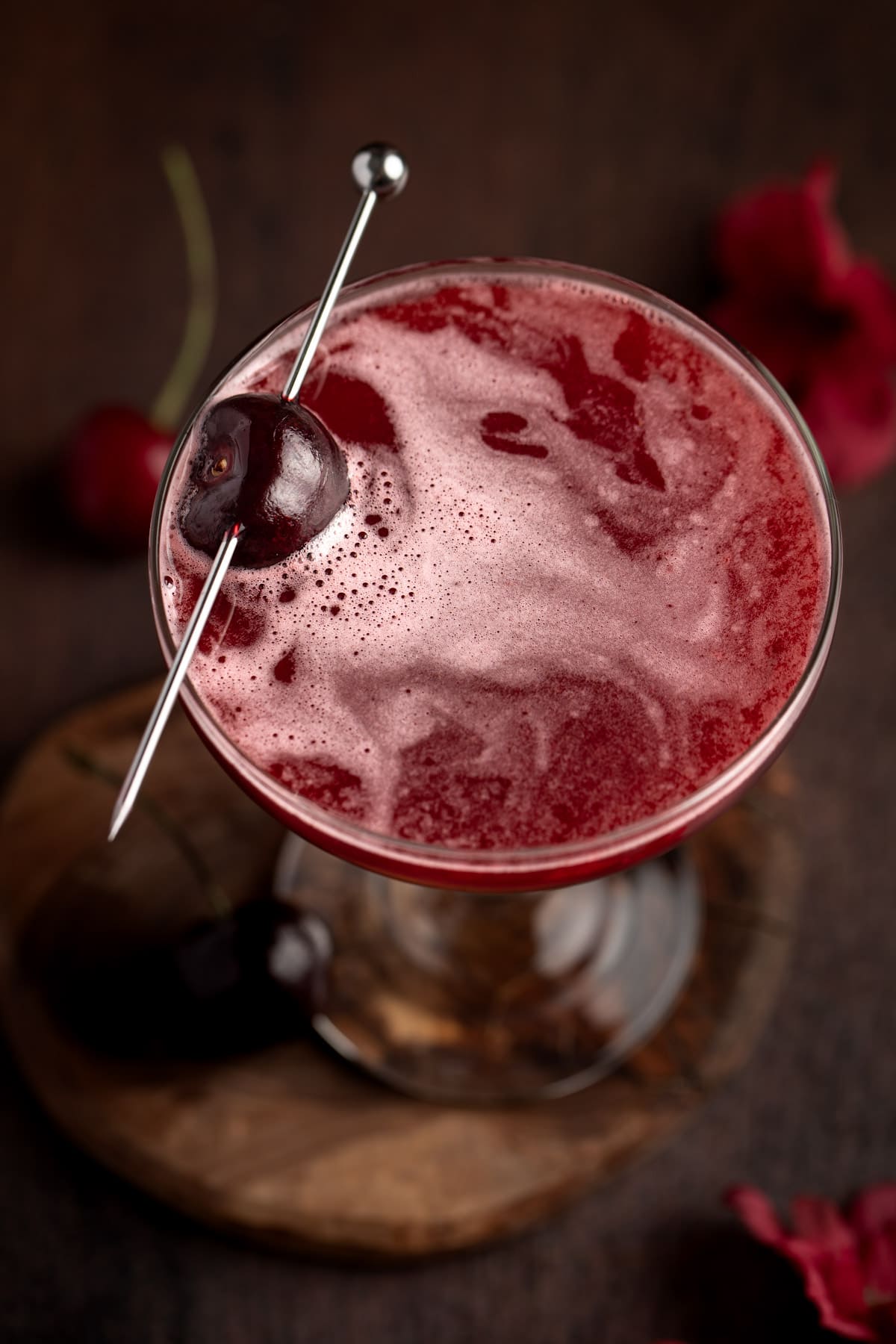 Overhead view of a red bourbon cherry cocktail on a wooden table.