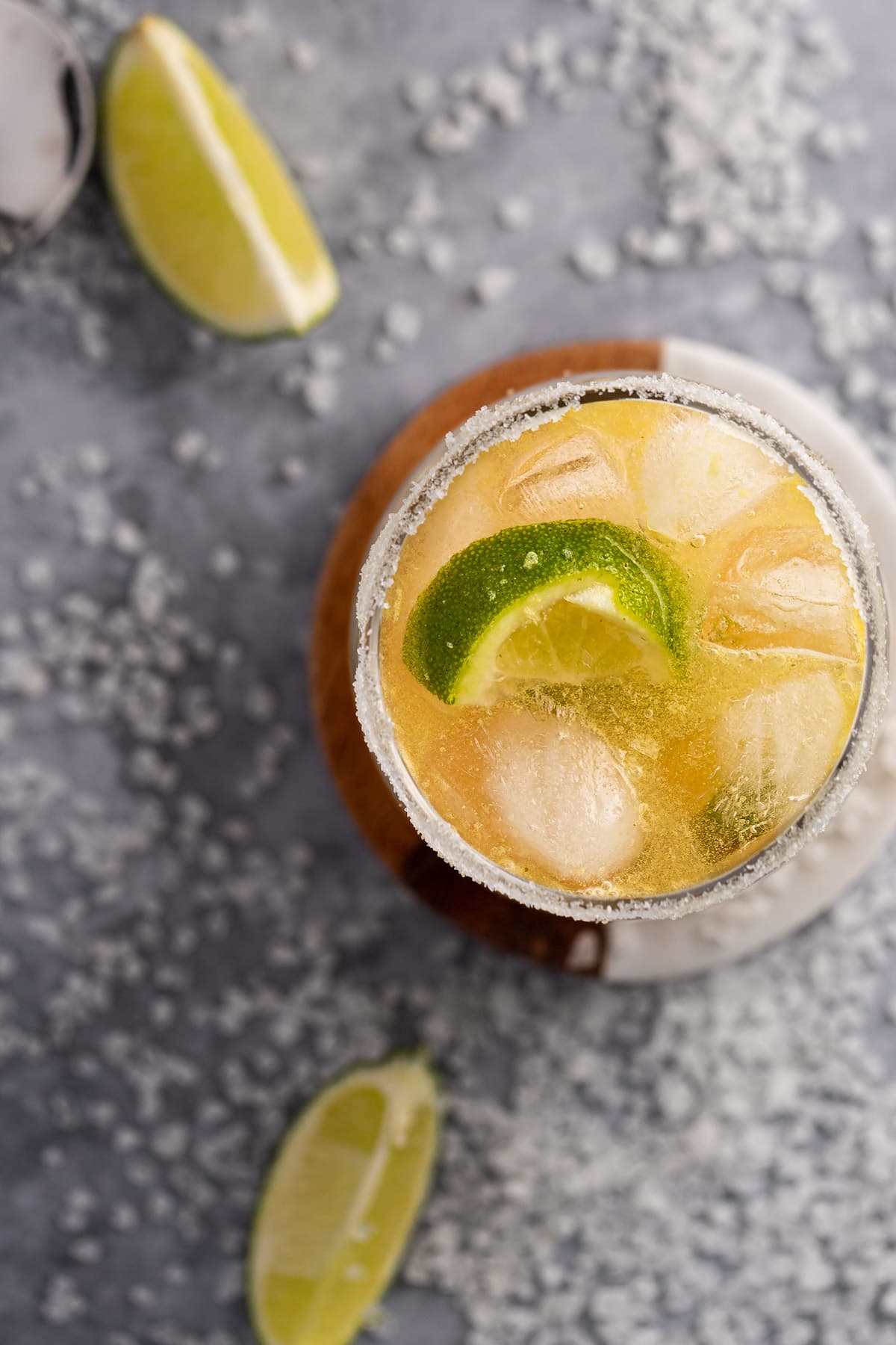 Overhead view of a margarita made with whiskey, on a table scattered with lime slices and salt.