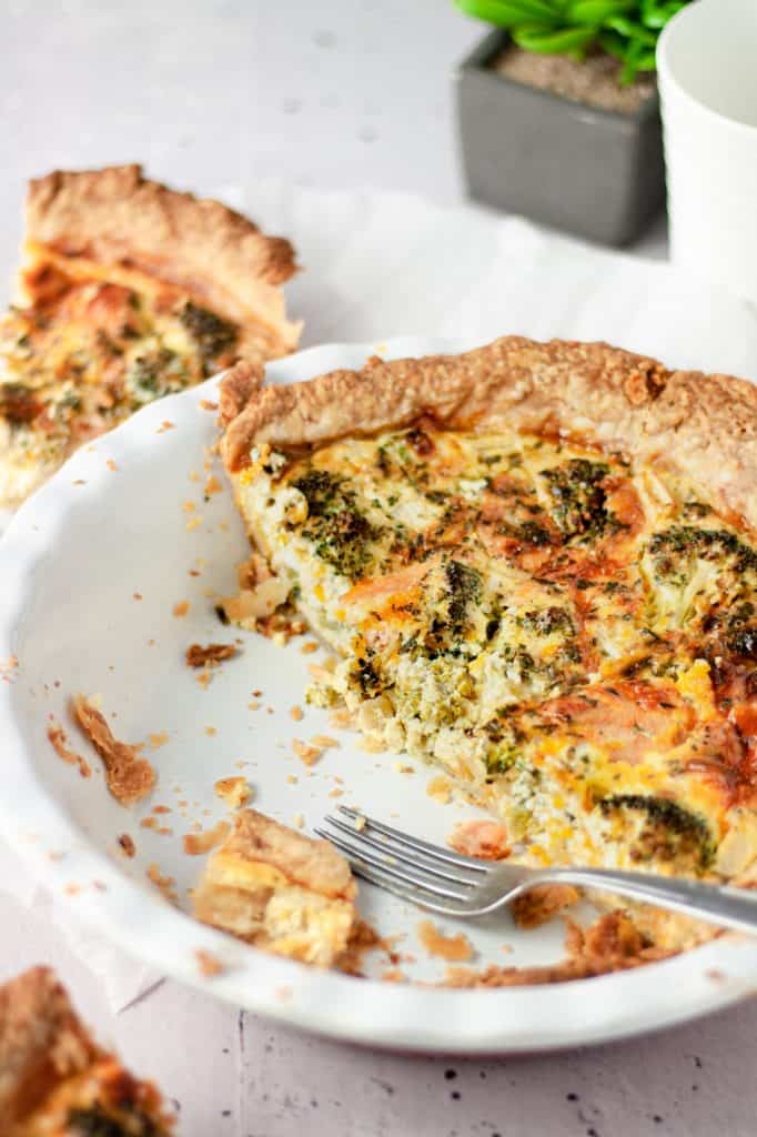 A half eaten broccoli and a smoked salmon pie in a white pie dish