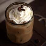 Brown cow drink topped with whipped cream and coffee beans, on a wooden table.