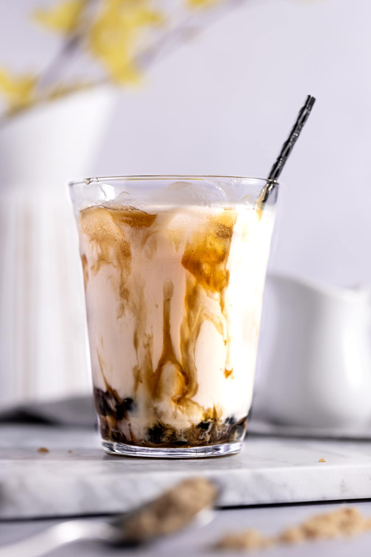 Up close of a glass of brown sugar milk tea with the brown sugar dripping down the sides as it mixes in with the milk and cooked boba pearls.