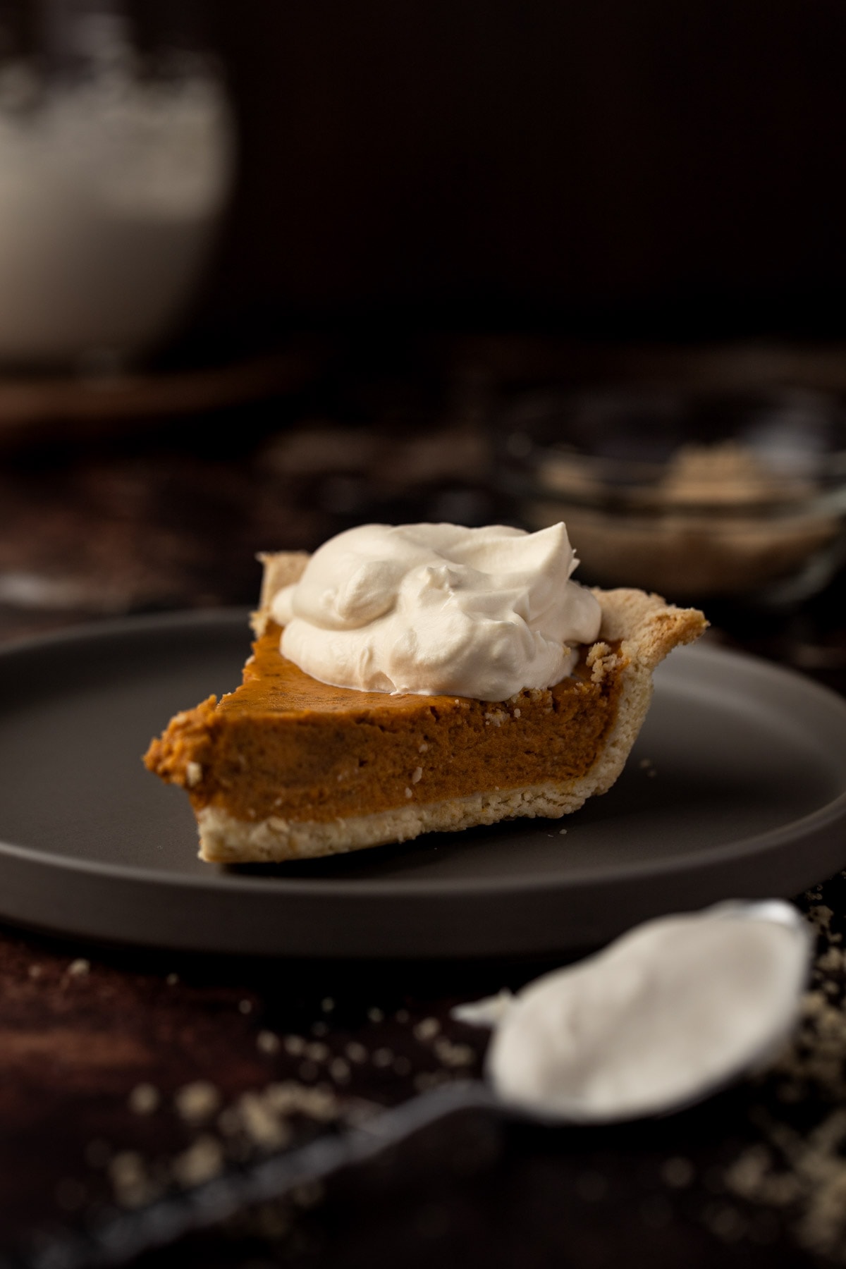 A slice of pumpkin pie with a dollop of whipped cream, on a dark brown round plate.