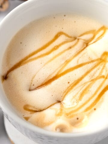 Overhead view of a caramel cappuccino topped with foam and a drizzle of caramel sauce.