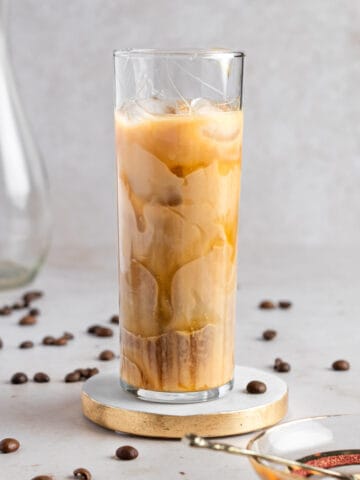 An iced caramel iced coffee in a tall glass, on a white marble table with coffee beans.