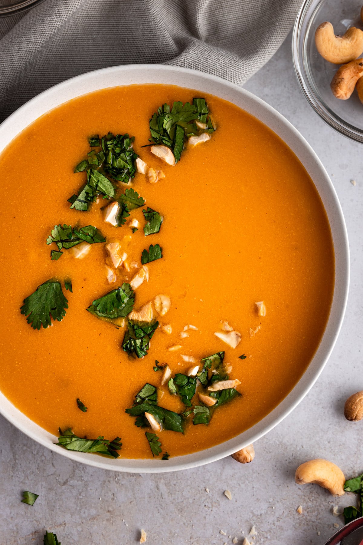A bowl of cashew carrot ginger soup garnished with fresh cilantro and crushed cashews.