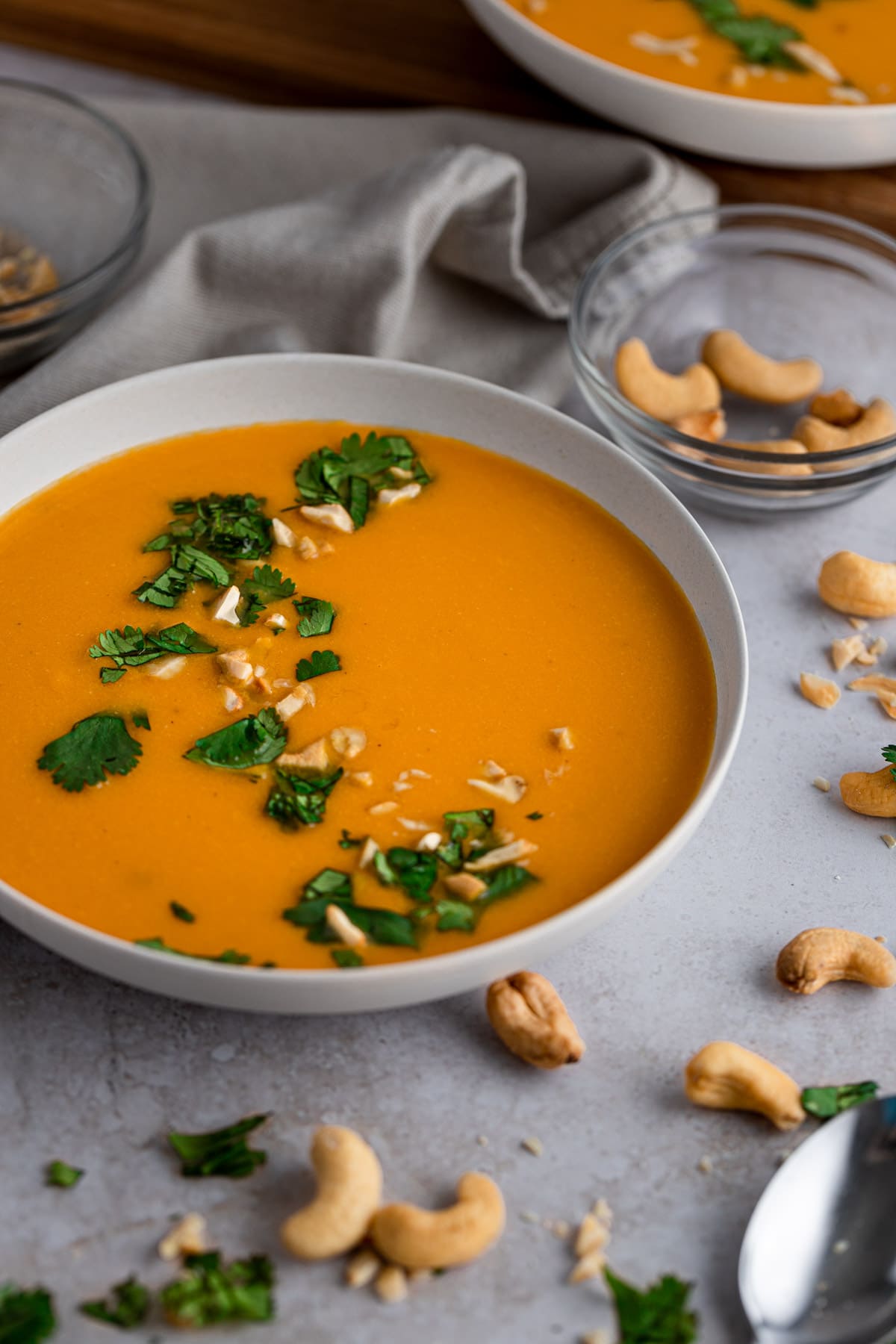 A bowl of vegan cashew ginger carrot soup topped with cilantro and cashews, with another bowl of soup in the background.