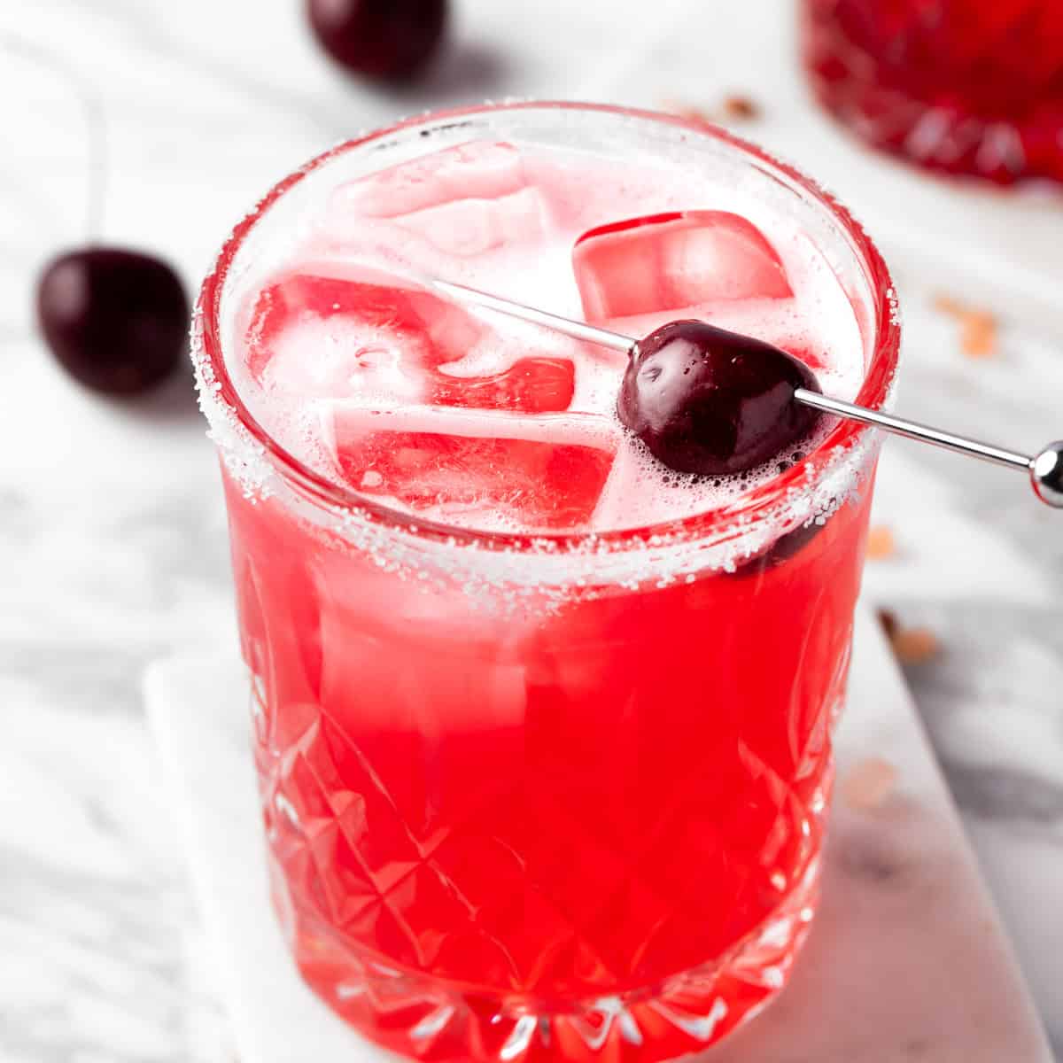 A red Cherry Limeade Margarita garnished with a dark cherry.