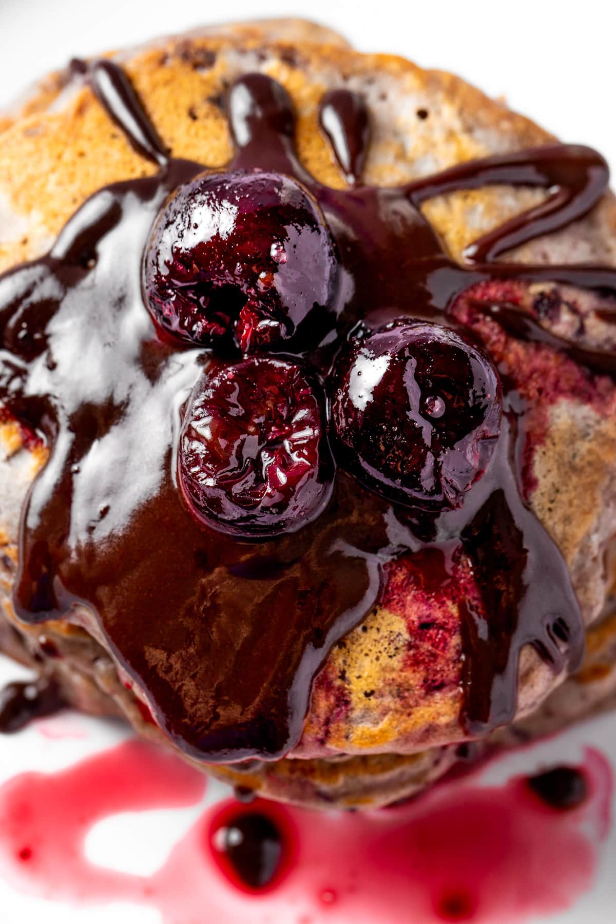 Cherry pancakes topped with chocolate sauce, cherry sauce and three round cherries.