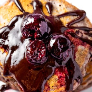 Cherry pancakes topped with chocolate sauce, cherry sauce and three round cherries.