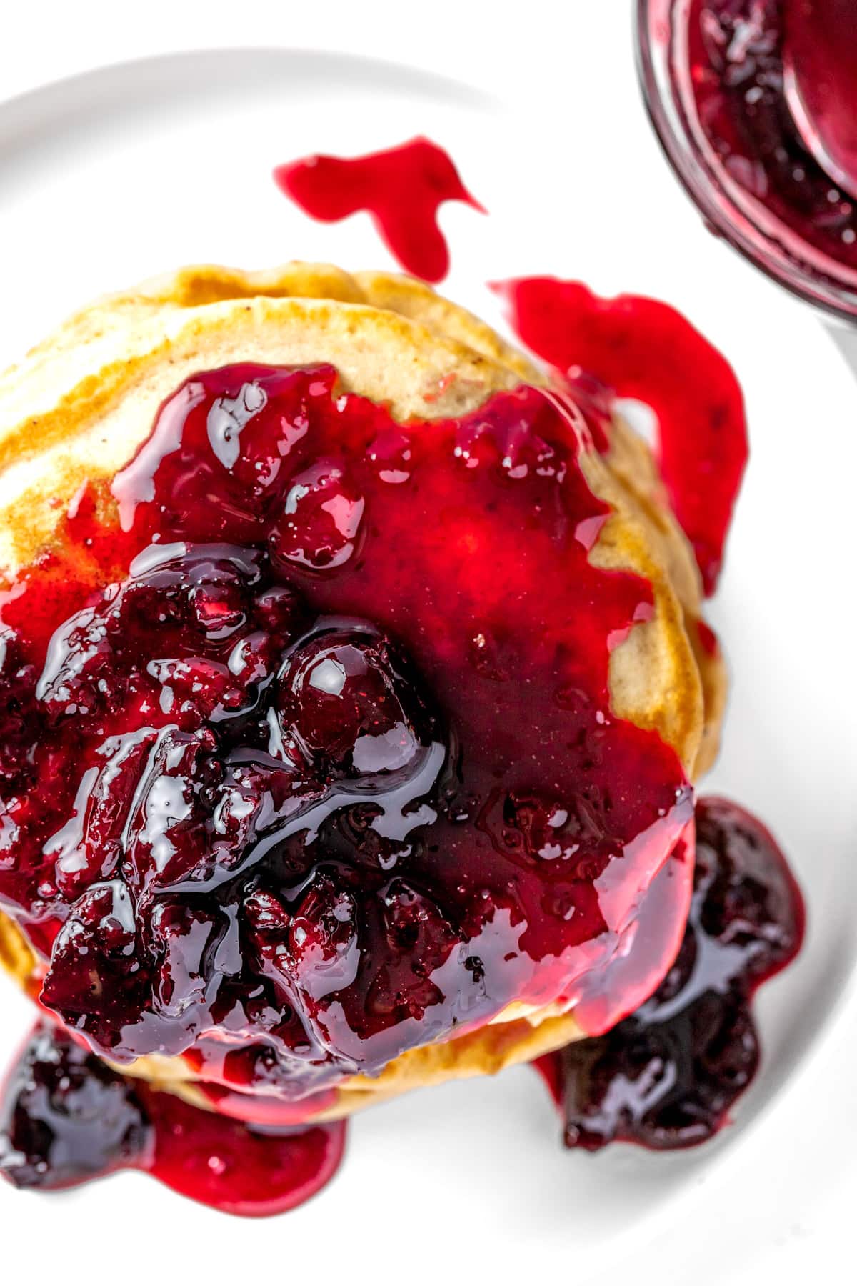 Overhead view of a stack of pancakes, topped with red cherry syrup.