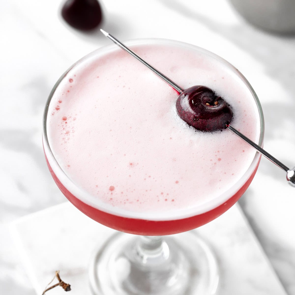 A cherry whiskey sour cocktail garnished with a fresh cherry.