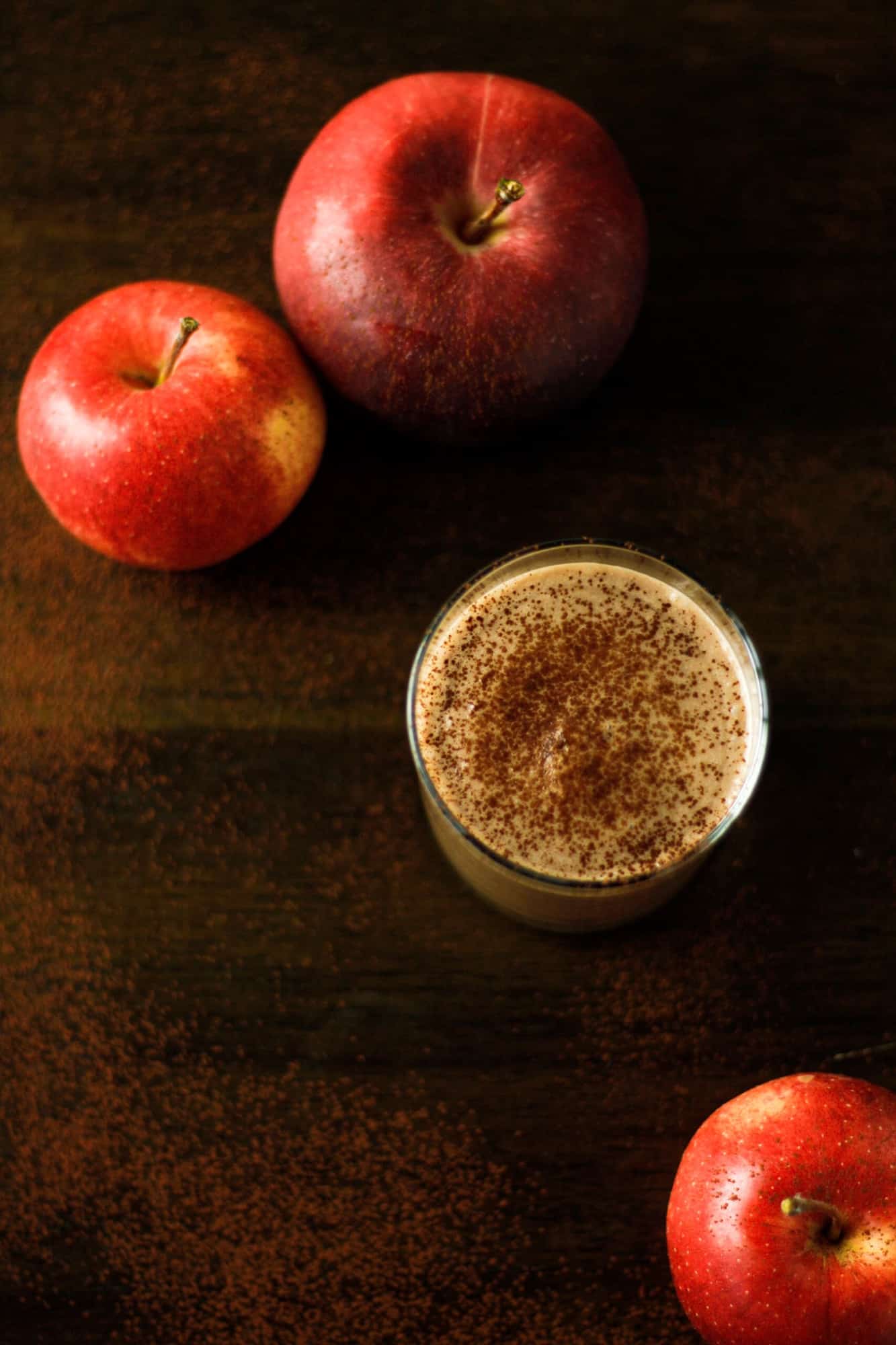 Overhead view of a chocolate apple smoothie on a wooden table, topped with a sprinkled of cinnamon.