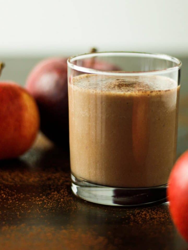 A glass of chocolate apple smoothie on the table next to three apples.