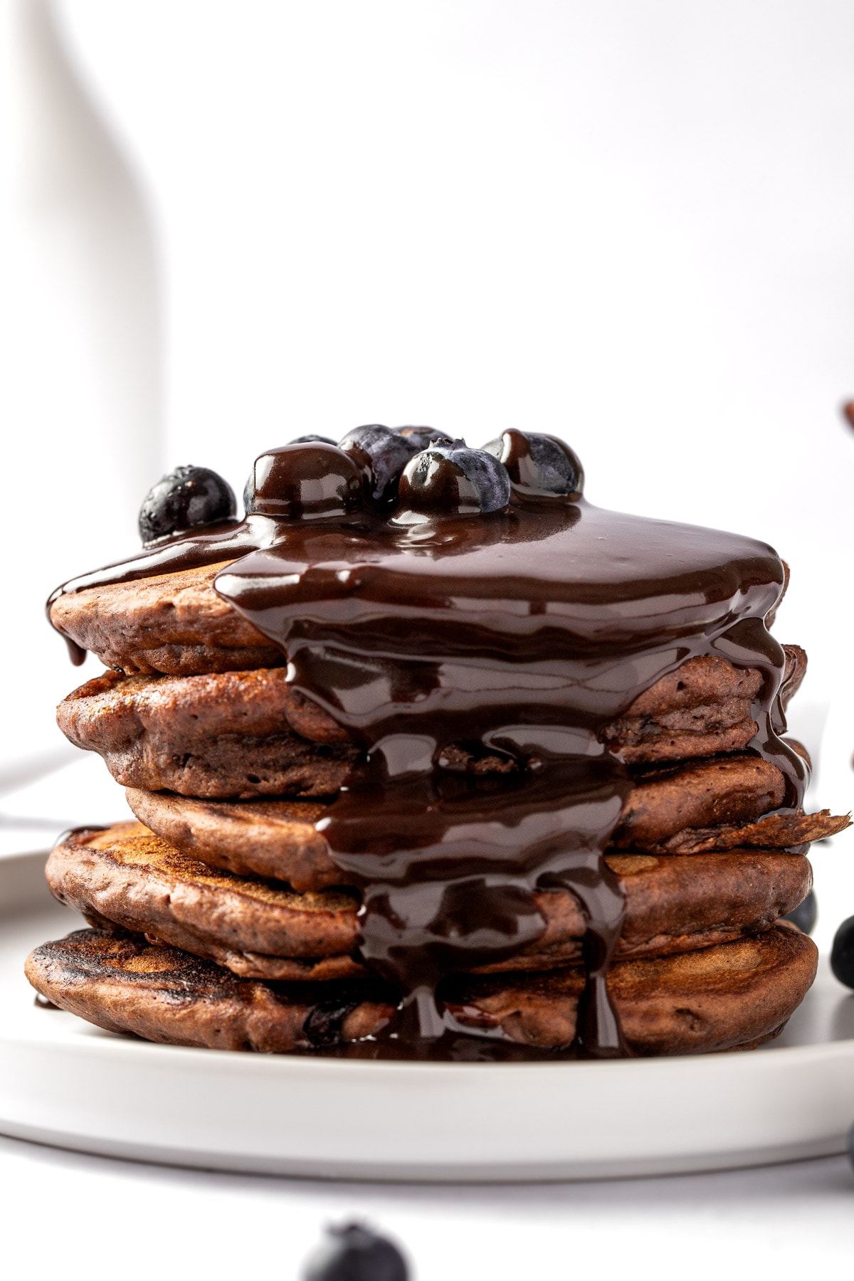 Eye level view of a stack of chai spiced pancakes drizzled with chocolate sauce, on a white plate.