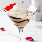 A chocolate cherry martini topped with whipped cream and garnished with maraschino cherries.