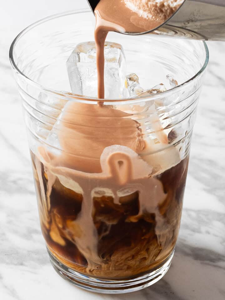 Chocolate cream cold foam being poured on top of cold brew coffee.