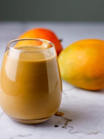 Glass of chocolate mango smoothie on table with mangoes in background