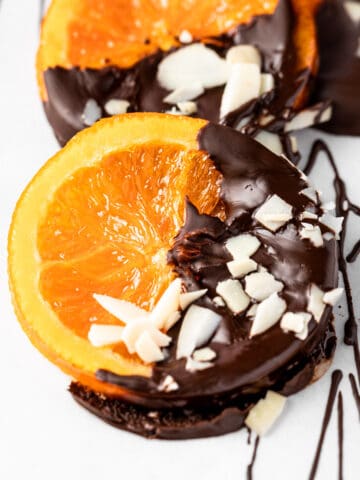 Chocolate orange slices dipped in chocolate, and topped with sliced almonds, sitting on a tray lined with parchment paper.