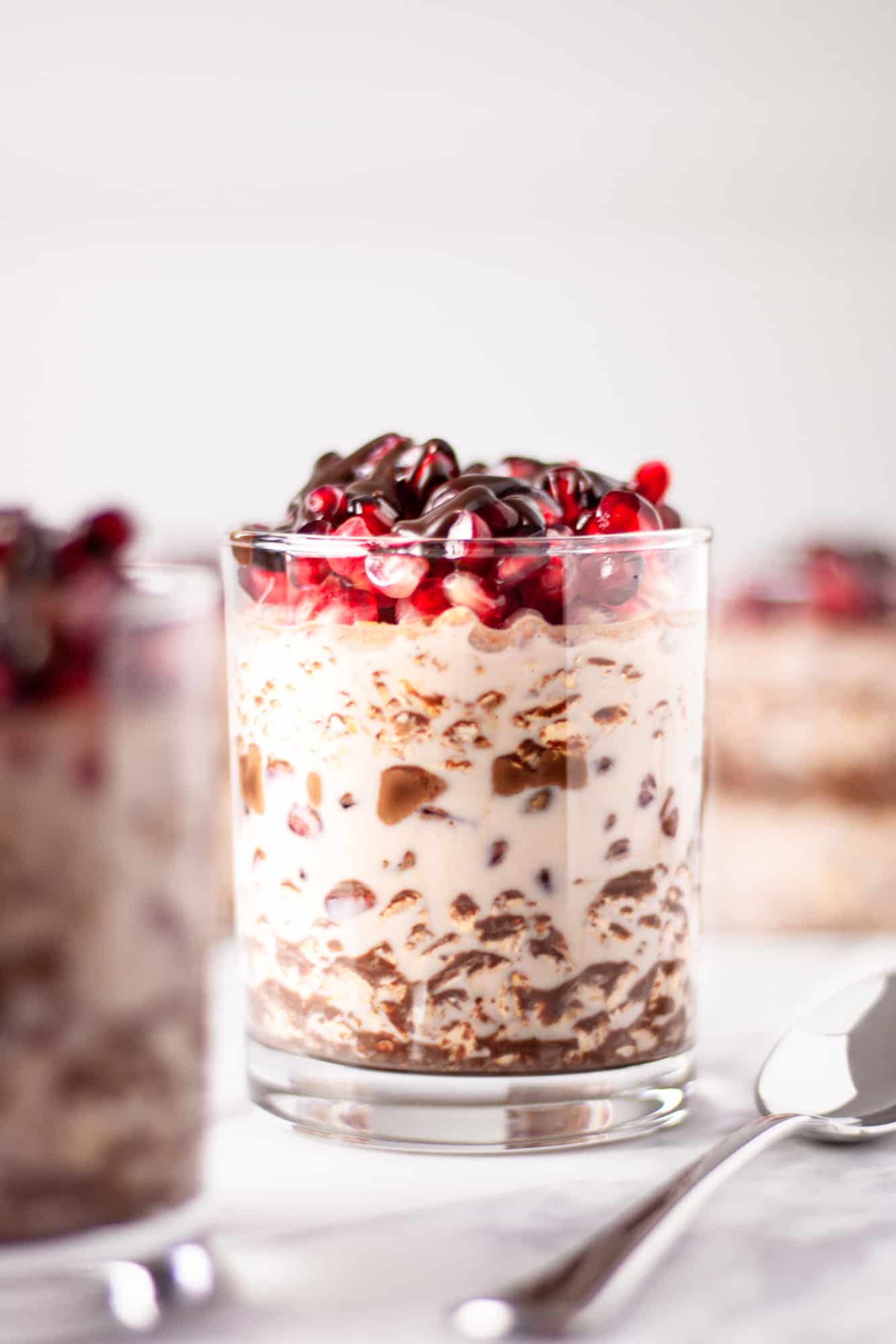 A glass of pomegranate overnight oats on a white table with other jars of overnight oats in the background.