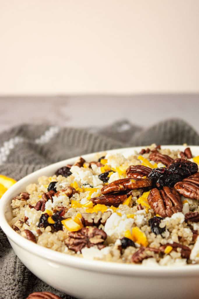Side view of a white bowl of cranberry pecan quinoa salad on a grey hand towel