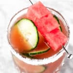 Overhead view of a cucumber watermelon margarita garnished with watermelon cubes and slices of cucumber.