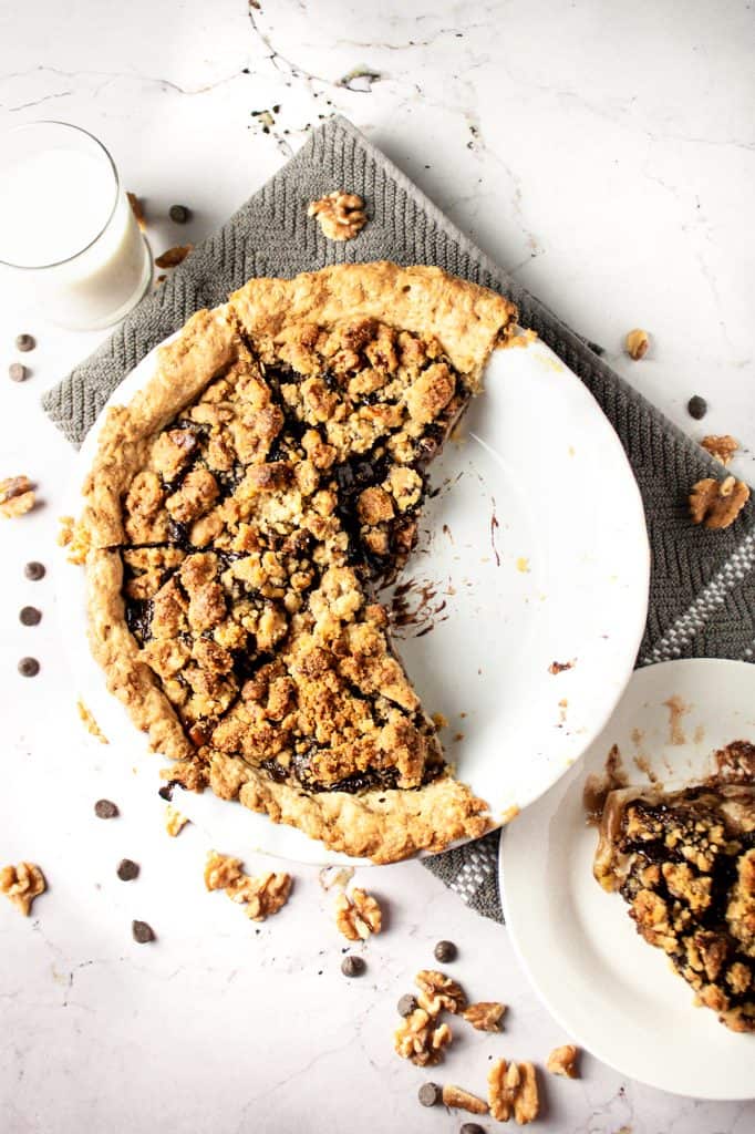 Overhead view of pear chocolate crumble pie with a couple slices missing, next to a glass of milk, on a marble white background with a grey hand towel