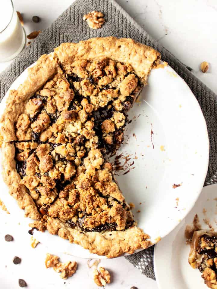 Overhead view of pear chocolate crumble pie with a couple slices missing, next to a glass of milk, on a marble white background with a grey hand towel