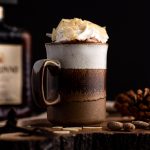 Side view of a brown mug of dark hot chocolate with amaretto, topped with whipped cream and sliced almonds, in front of a black background.