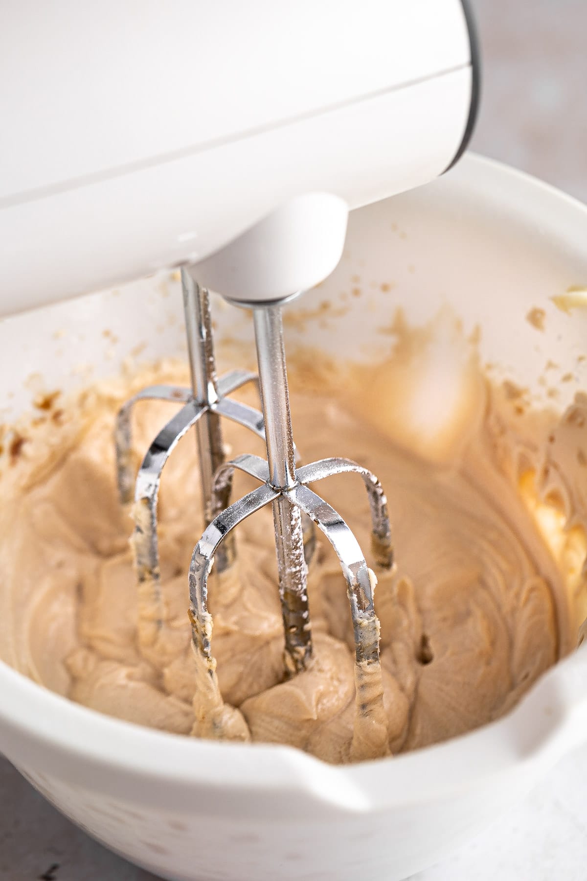 Espresso frosting being mixed with a handheld mixer in a white bowl.