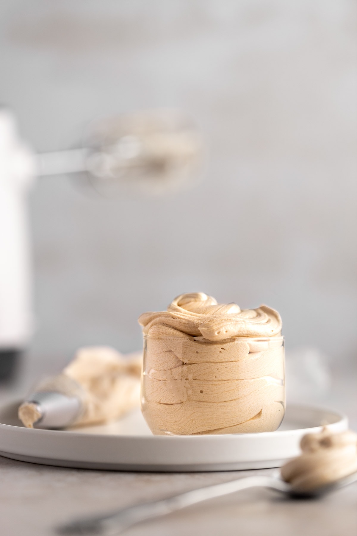 Espresso buttercream frosting in a small glass jar, on a white plate.