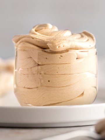 Espresso buttercream frosting in a small glass jar, on a white plate.