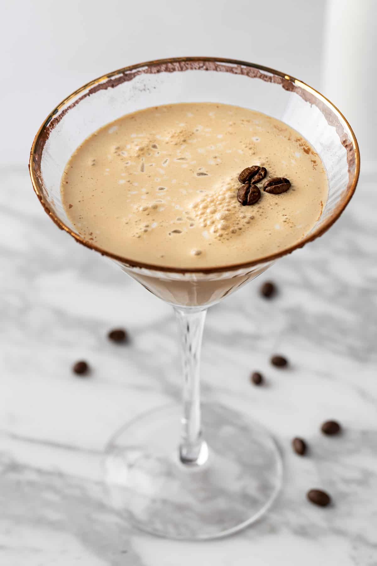 An espresso martini mocktail garnished with a cocoa rim and 3 coffee beans.