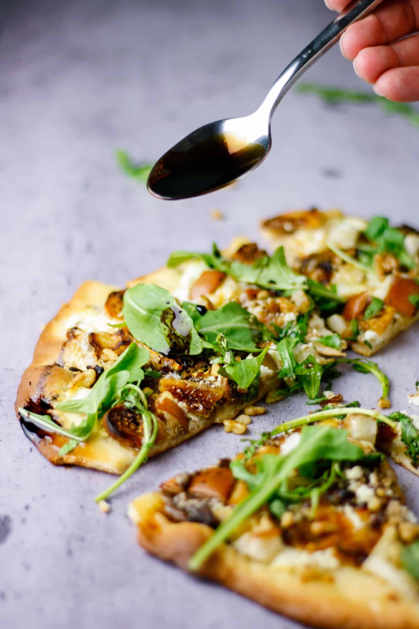 spoon drizzling balsamic glaze over fig, pear, walnut, brie, honey and goat cheese pizza