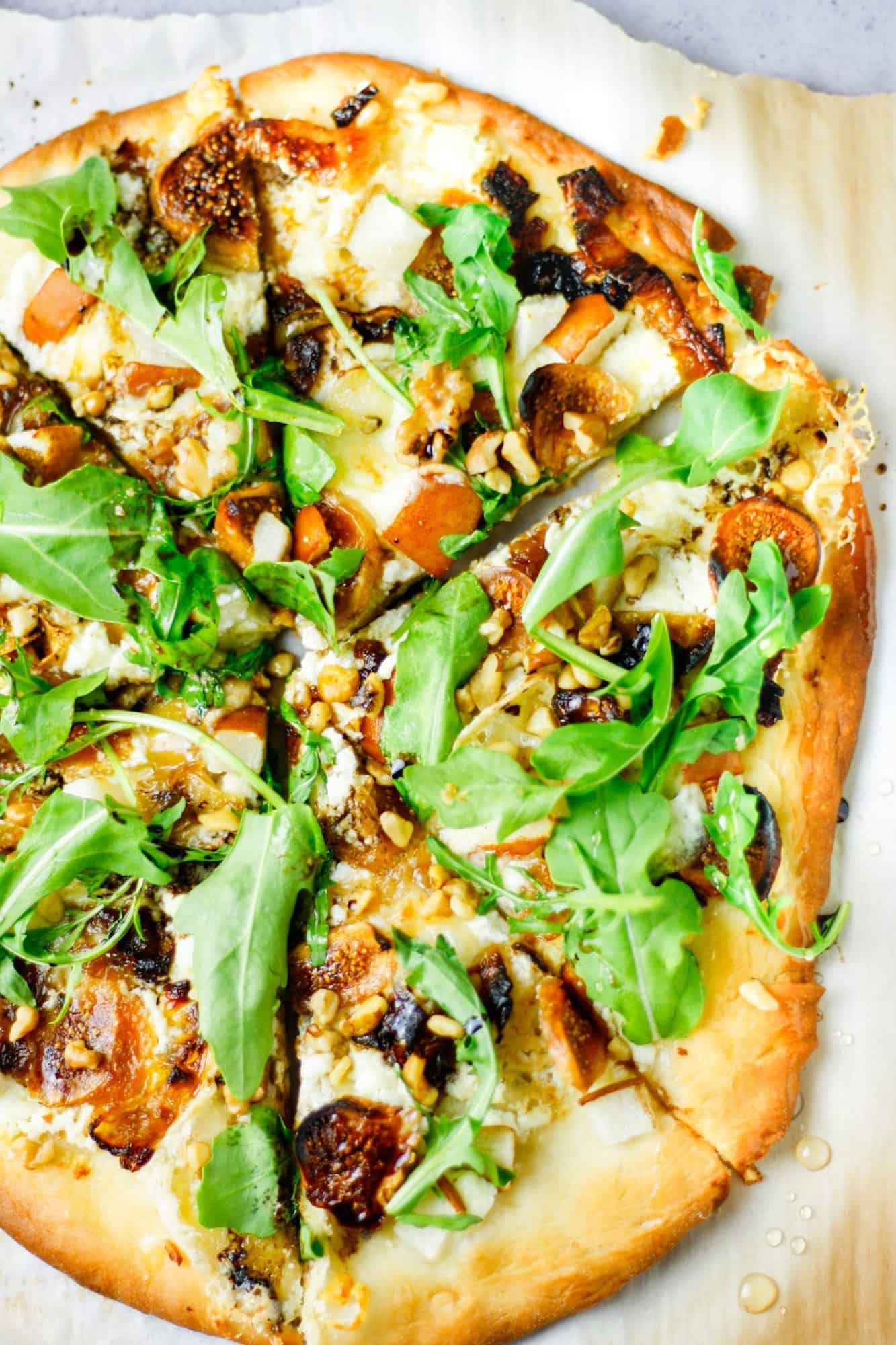 Overhead view of whole fig, pear, walnut, brie, honey and goat cheese pizza cut into slices.