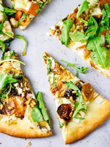Fig, pear, walnut, brie, honey and goat cheese pizza slices spread out on table