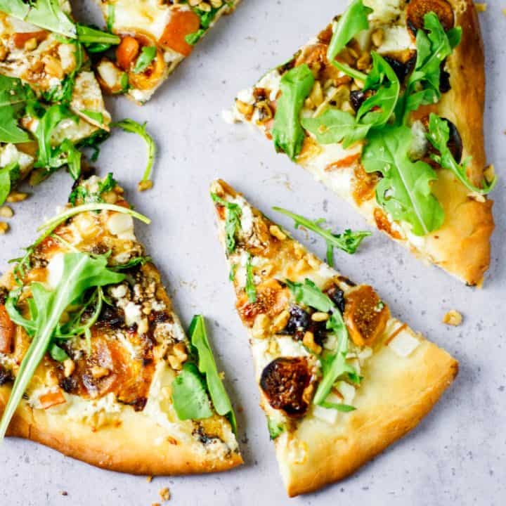 Fig, pear, walnut, brie, honey and goat cheese pizza slices spread out on table