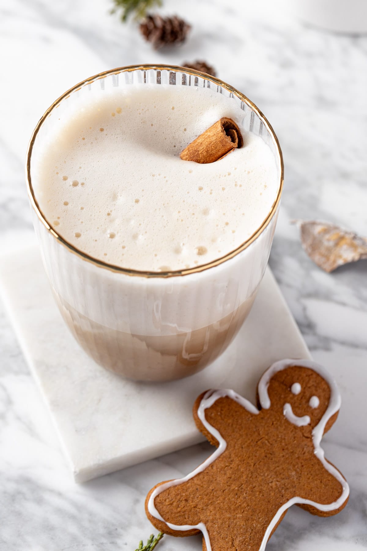 A gingerbread chai latte garnished with a cinnamon stick, on a white marble coaster.