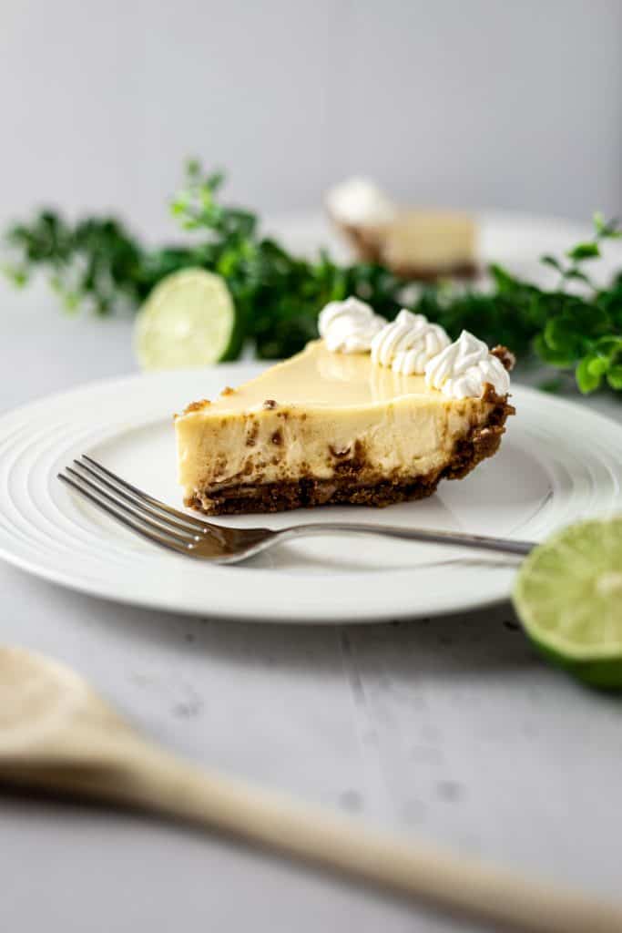 Up close view of a slice of gluten free key lime pie with whipped cream on top and limes and green garland in the background