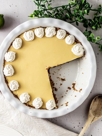 Overhead view of a gluten free key lime pie with a piece cut out from it, decorated with whipped cream dollops along the edges