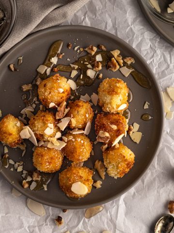 Goat cheese croquettes drizzled with honey, almonds and walnuts, on a dark grey plate.