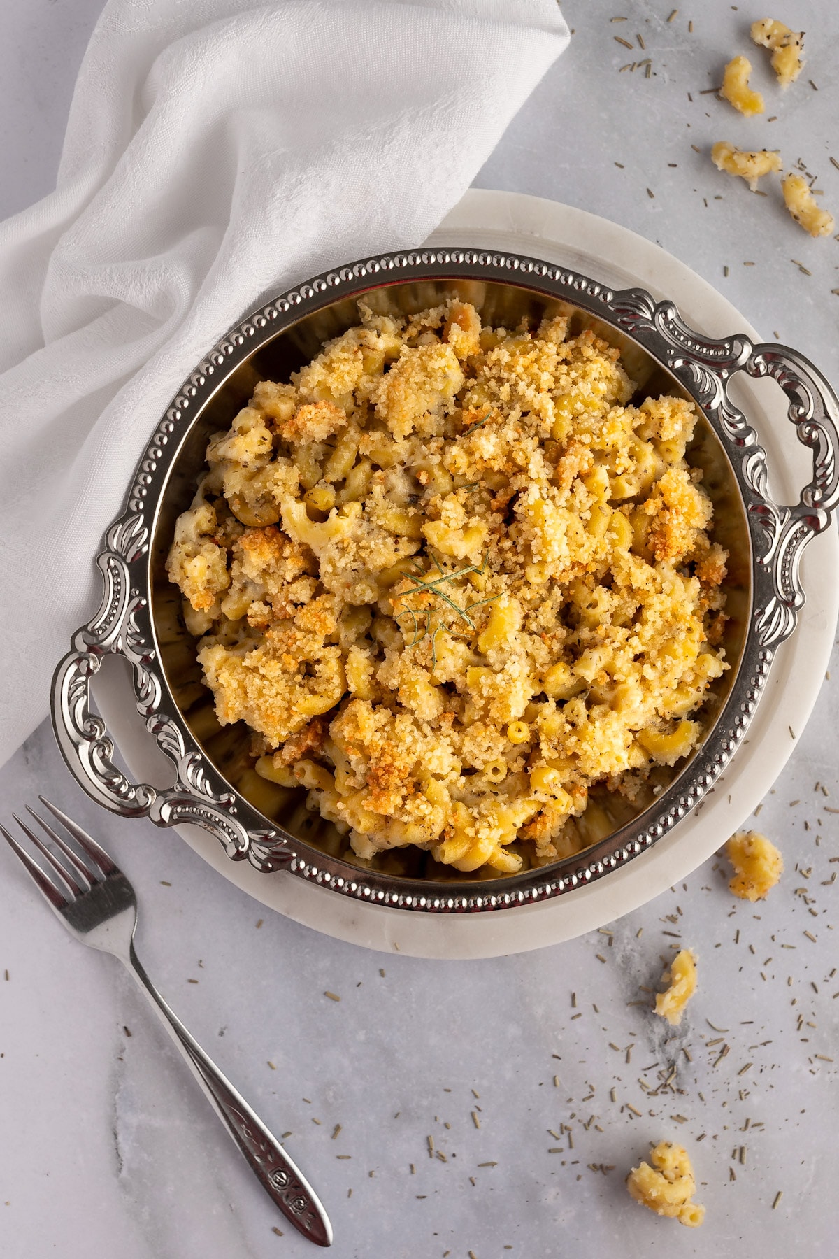 Overhead view of goat cheese mac and cheese in a round, decorative metal serving tray, on a white marble background.