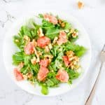 Overhead view of a plate of grapefruit arugula salad on a marble table with a fork on the side.
